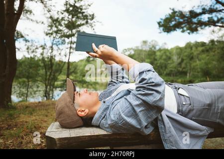 Young woman reading book while lying on wooden bench Stock Photo