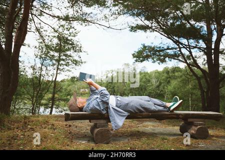Young woman reading book while lying on wooden bench Stock Photo