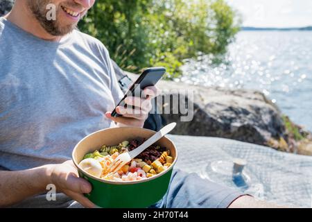 Man holding bowl with food and using phone Stock Photo