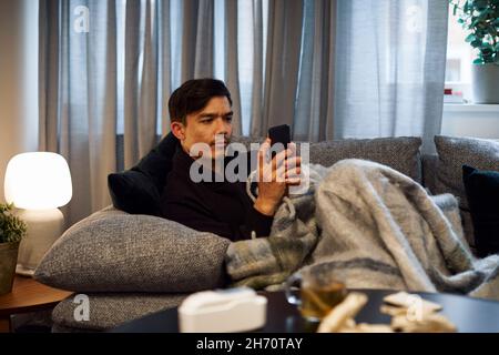 Young man sitting on sofa and using smart phone Stock Photo