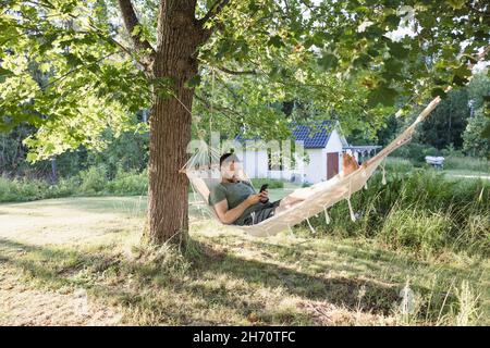 Man lying in hammock in garden and using phone Stock Photo
