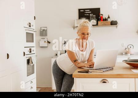 Woman using laptop in kitchen Stock Photo