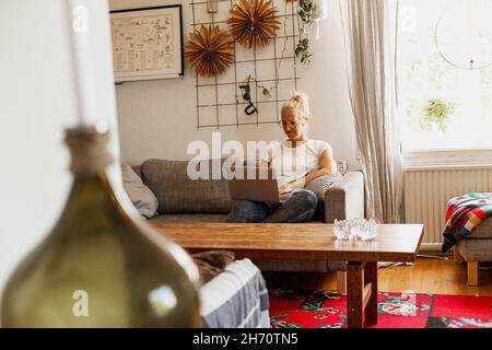 Smiling woman using laptop on sofa Stock Photo