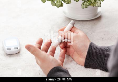 man hands using lancet on finger to check blood sugar or ketones level by glucose meter. medicine diabetes keto diet health care at home Stock Photo