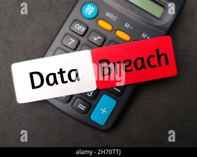 Colored wooden board written with text Data Breach with calculator on black background. Stock Photo