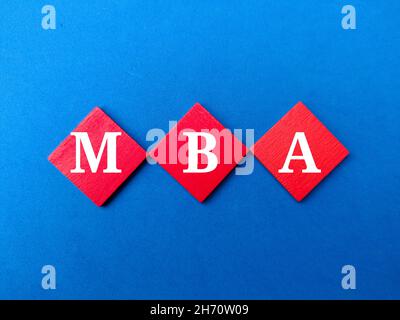 Colored wooden cube written with text MBA on blue background. Stock Photo
