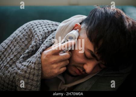 Ill man on sofa checking temperature Stock Photo