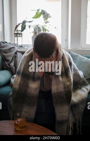 Ill man on sofa with face in hands Stock Photo
