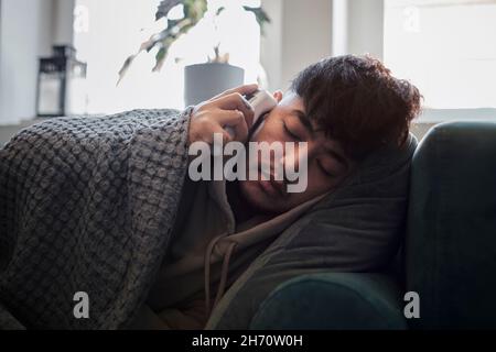 Ill man on sofa checking temperature Stock Photo