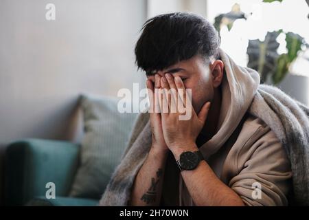 Ill man on sofa with hands covering face Stock Photo