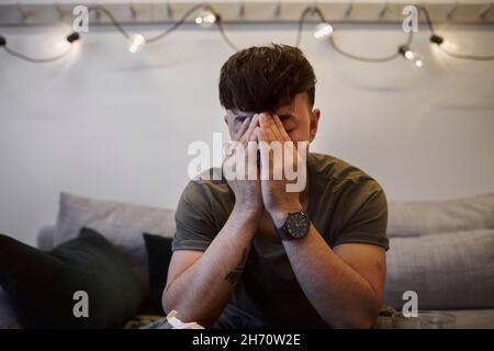 Ill man on sofa with face in hands Stock Photo