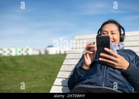 Young woman with smartphone relaxing on wooden sun chair Stock Photo