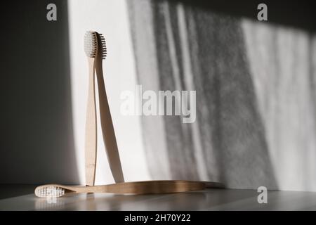 two light wood bamboo eco recyclable toothbrushes standing vertical and lying horizontal with white bristles on white background and morning shadows Stock Photo