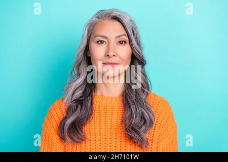 Portrait of attractive content calm grey-haired woman wearing orange pullover isolated over bright teal turquoise color background Stock Photo