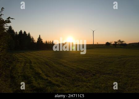 Wind turbine on a hill in front of a field and at the edge of the forest at sunset. Renewable energy belongs to the future and helps against climate c Stock Photo