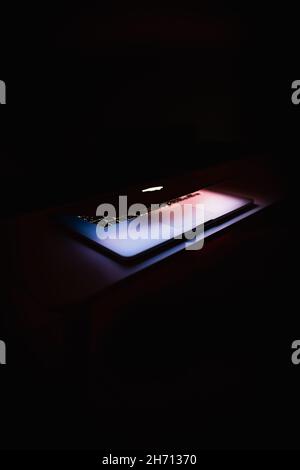 TRUTNOV, CZECH REPUBLIC - Nov 18, 2019: A half-closed MacBook laptop glowing brightly, surrounded by darkness in a pitch-black room Stock Photo