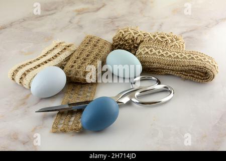 Blue Easter eggs, textured ribbons, and scissors on table for crafting project for Easter holiday Stock Photo