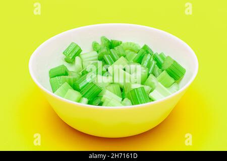 Fresh Chopped Celery Pieces with Water Drops in White Bowl on Yellow Background. Vegan and Vegetarian Culture. Raw Food. Healthy Diet with Negative Calorie Content Stock Photo