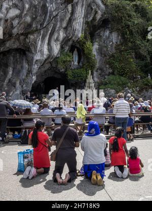 Lourdes, France - August 28, 2021: Pilgrims praying in front of the cave of apparitions of holy Mary in Lourdes Stock Photo