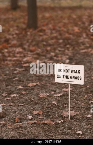 White sign with the inscription in English "do not walk on the grass" on a blurry autumn background with trees and fallen leaves Stock Photo