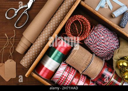 Christmas Flat Lay - Box of Christmas present wrapping supplies with wrapping paper and gift tags on a dark rustic wood table. Stock Photo