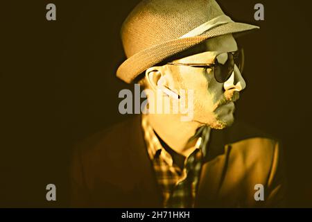middle-aged man in a hat and aviator glasses, in wireless headphones, in yellow tones Stock Photo