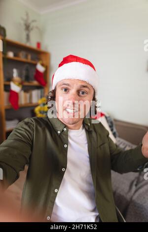 Portrait of caucasian disabled man in santa hat sitting on a wheelchair at home during christmas Stock Photo
