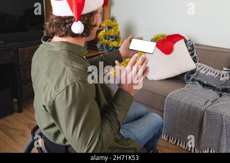 Caucasian disabled man in santa hat using smartphone with copy space at home during christmas Stock Photo