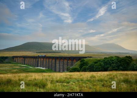 Scenic countryside valley (locomotive on landmark Ribblehead Viaduct, sunlight on arches, high hills & mountain) - North Yorkshire Dales, England UK. Stock Photo