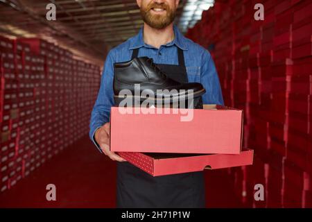 Warehouse worker or owner of a shoe making factory showing a new black leather boot Stock Photo