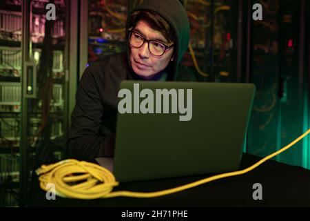 Asian male hacker using a laptop in computer server room Stock Photo