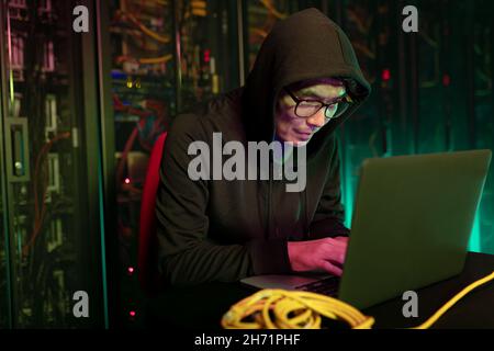 Asian male hacker using a laptop in computer server room Stock Photo