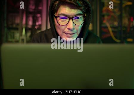 Asian male hacker using a laptop in computer server room Stock Photo