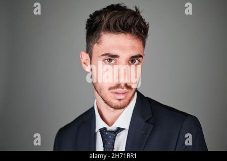 Young man close up portrait wearing a dark blue suit and a dark blue tie with red and light blue dots. Stock Photo