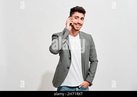 Happy young man wearing jeans, a white tshirt and a grey blazer talking with someone on his mobile phone Stock Photo