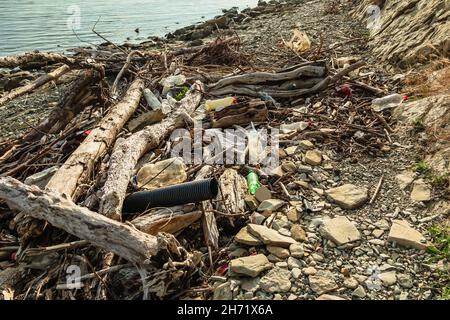 Logs, branches, plastic bottles and other debris are lying on the seashore. The stone beach is littered with garbage. The concept of ecology Stock Photo