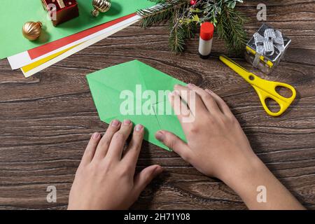 Instruction step 3. Christmas greeting card gift origami candle on wooden table. Childrens art project, handmade, crafts for kids. Stock Photo