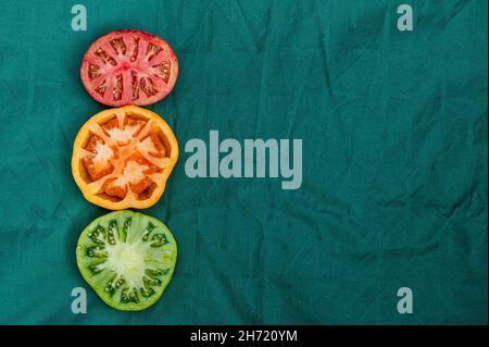red, yellow and green tomato halves on a green background, close-up from above, abstract semaphore Stock Photo