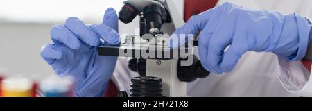 cropped view of scientist in latex gloves near microscope, banner Stock Photo