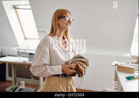 Smiling seamstress in glasses holds stack of cloth Stock Photo