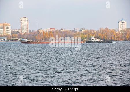 An articulated tug and bulk barge transport sand and construction materials along the river. A large barge sails along the wide Dnieper River. Transpo Stock Photo