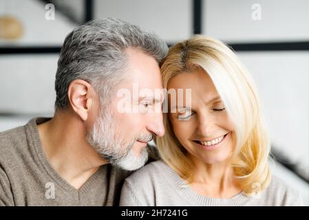 Headshot of romantic middle-aged couple indoors. Handsome grey-haired mature man watching with passion and love at beautiful charming mid-age woman. Mature spouses at home Stock Photo