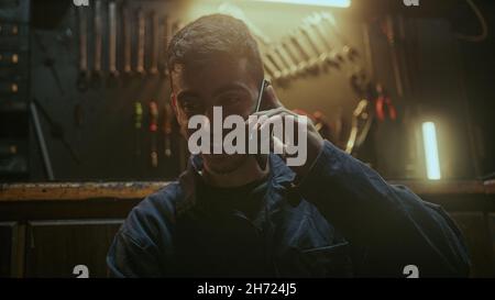 Handsome determined blacksmith man sitting in front of the workbench and he using smartphone call friends or her family Stock Photo