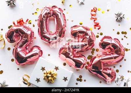 Pink balloons made of foil in the form of numbers 2022 with confetti and gift box on a white background.Celebrating Christmas, New Year and festive concept. Flat lay, top view. Stock Photo