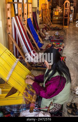 A Bhutanese woman weaving fabric on a wooden loom by hand in Bhutan. Stock Photo