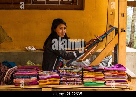 A Bhutanese woman weaving fabric on a wooden loom in front of her house in Thimphu, Bhutan. Stock Photo