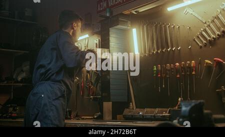 Male young blacksmith man putting his tools and equipment in place in his awesome looking workshop, back view Stock Photo