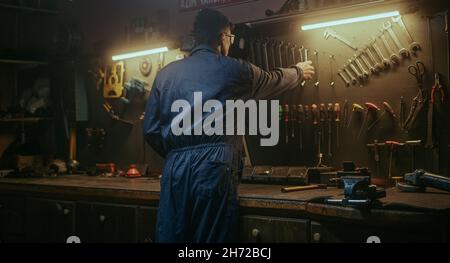 Young blacksmith male person picking up his tools from the bench to do work Stock Photo