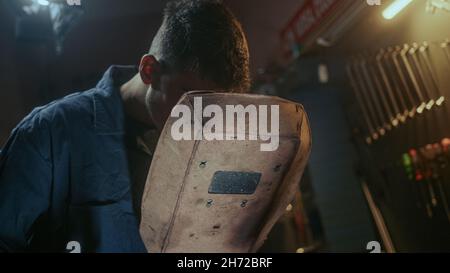 Young blacksmith male with welding shield using welding machine for welding metal construction on production workshop Stock Photo