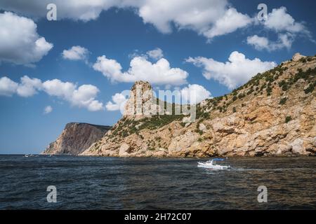 Tourist day trip pleasure boat moves along beautiful cliff landscape with white clouds in sky. Balaklava. Black sea Crimea Stock Photo